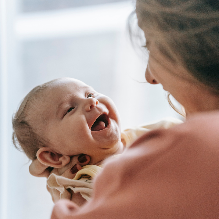 Image of a woman holding a baby and they are both smiling at each other
